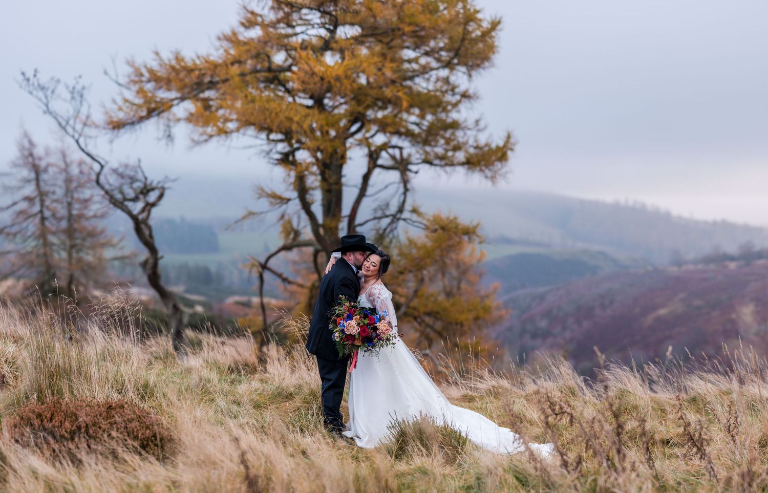 Aberdeen Wedding Photography. Wedding couple poses in autumn field with golden trees and mountain backdrop.