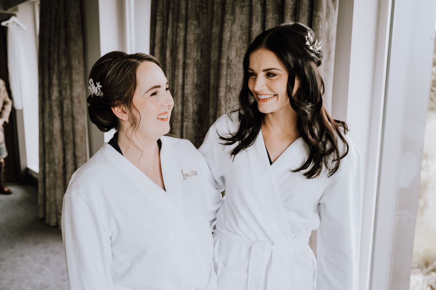 Two people in white robes sharing a moment during wedding preparations.