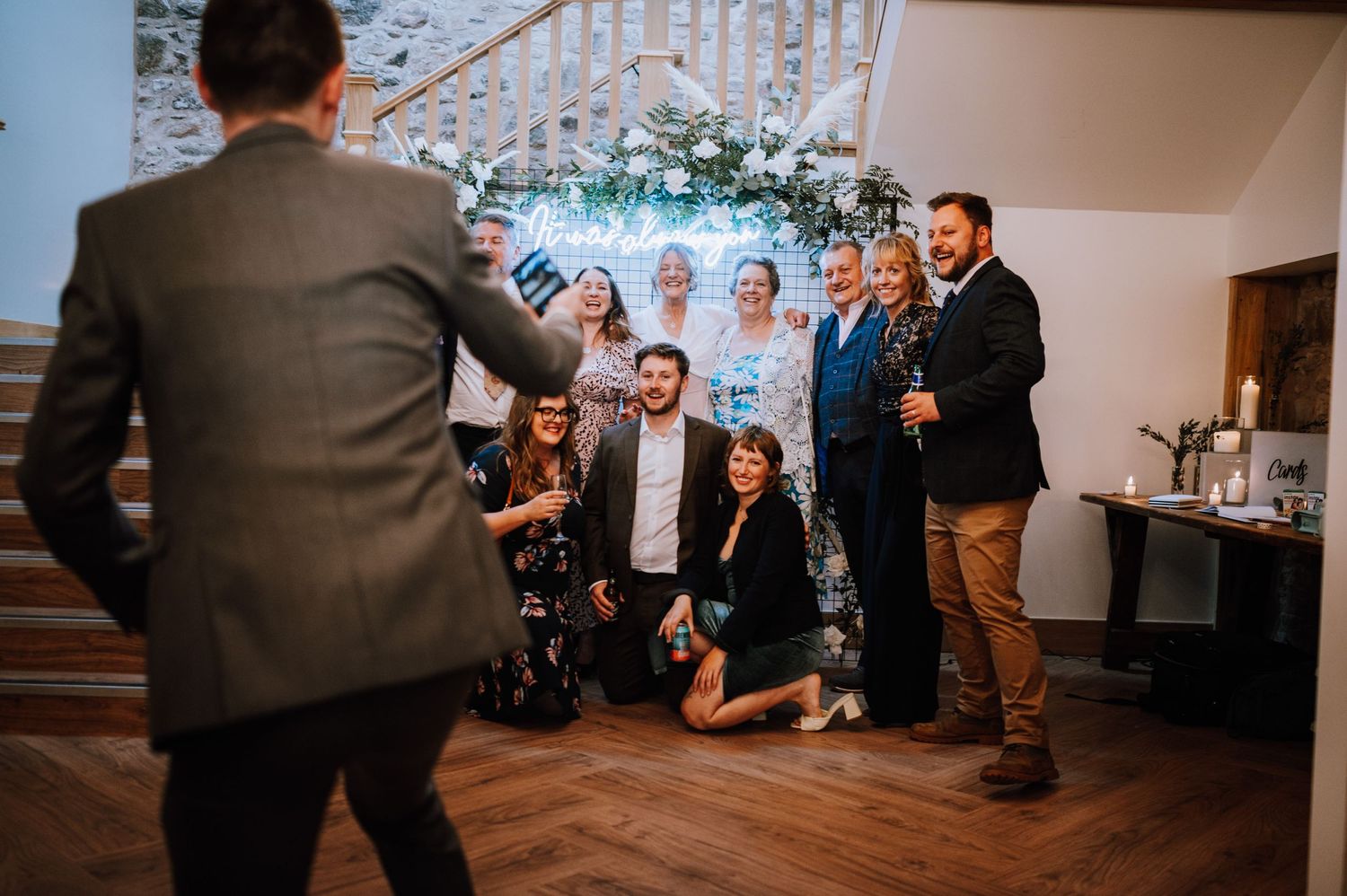 Group of wedding guests posing informally on wooden stairs at reception.