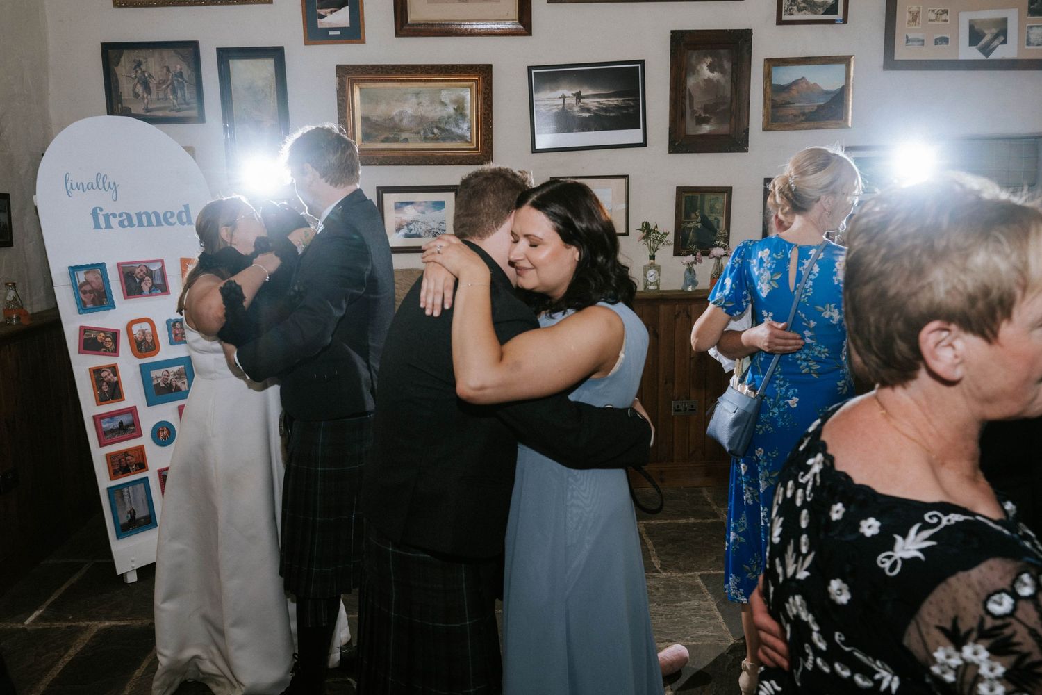 Wedding reception guests dancing and embracing on the dance floor surrounded by photo-covered walls.