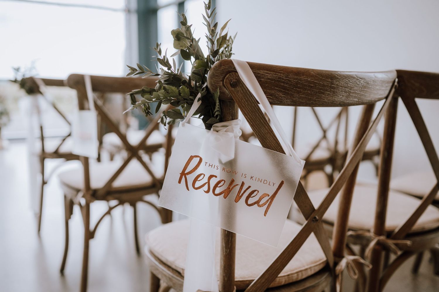 Wooden wedding ceremony chair with reserved sign and greenery decoration.