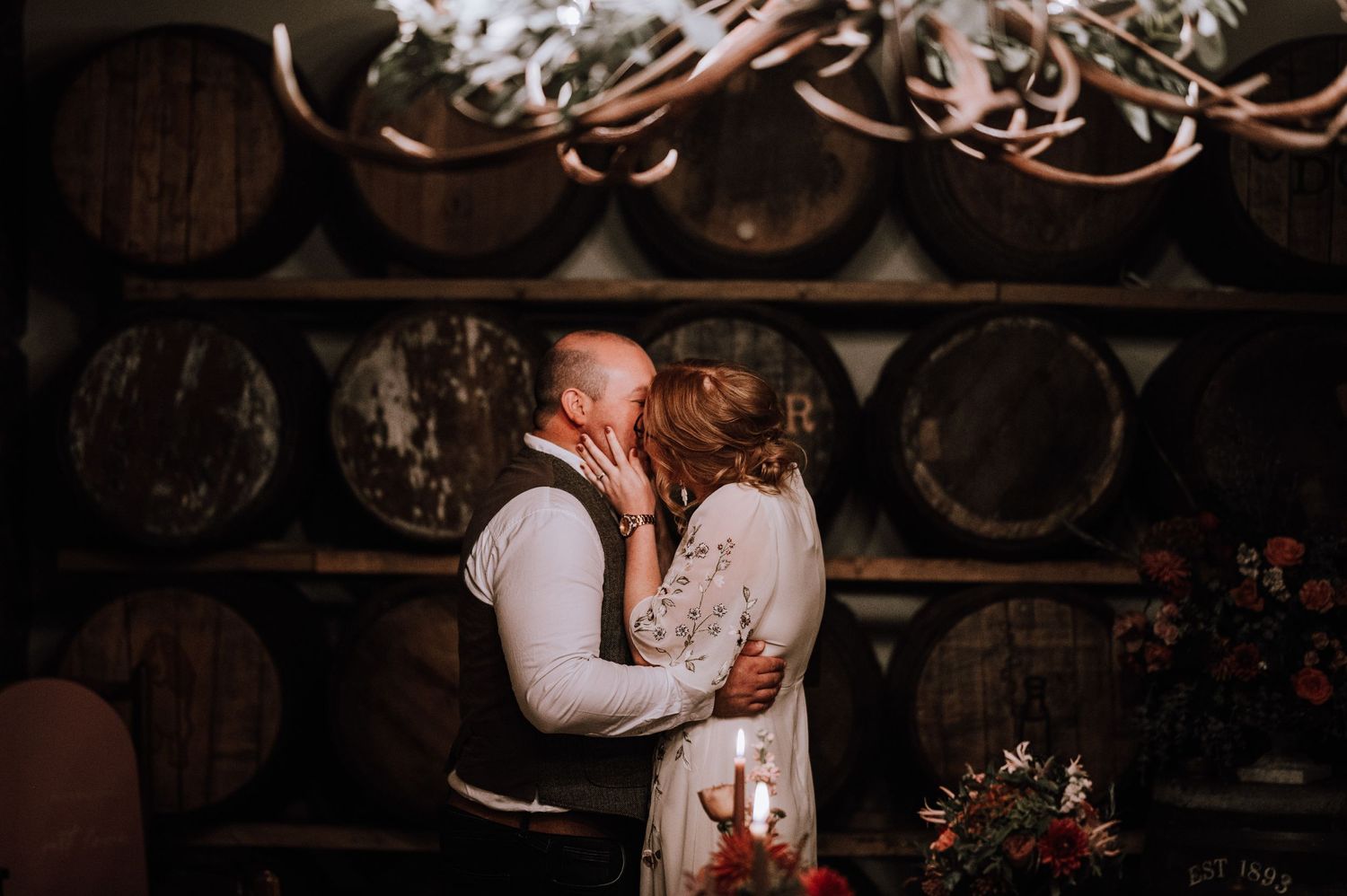 Romantic moment shared in front of stacked wine barrels and soft lighting.