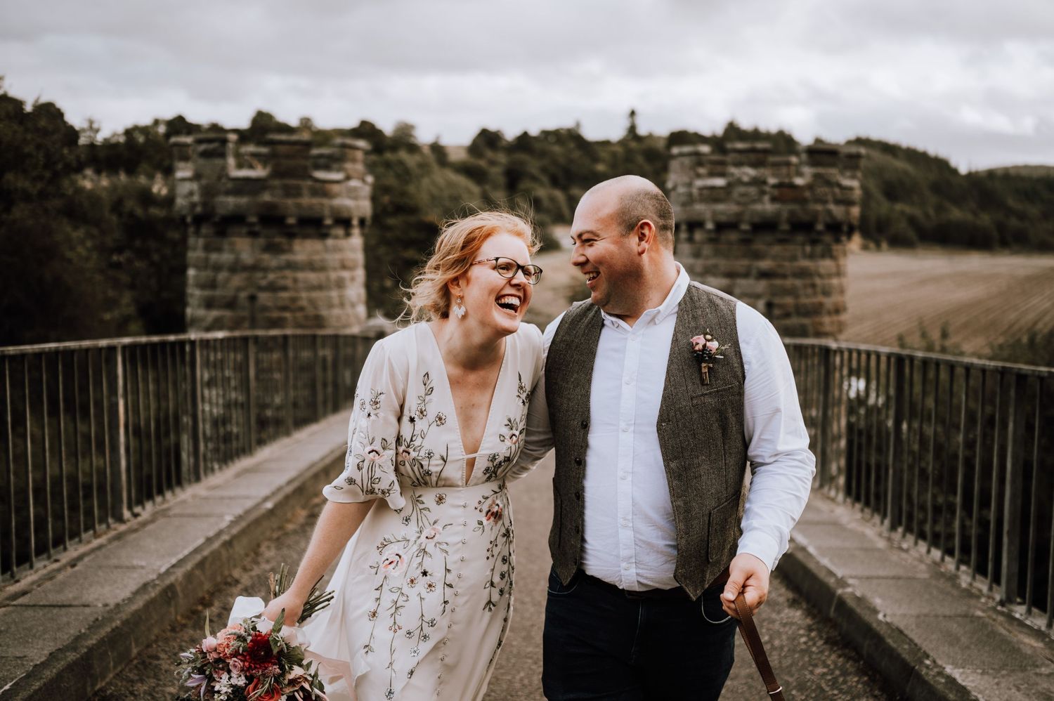 Candid moment shared on a historic stone bridge under cloudy skies.