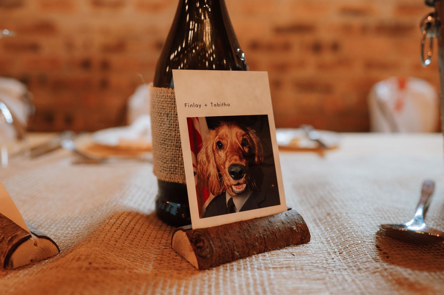 Place card holder with adorable dog photo displayed on textured tablecloth next to wine bottle.