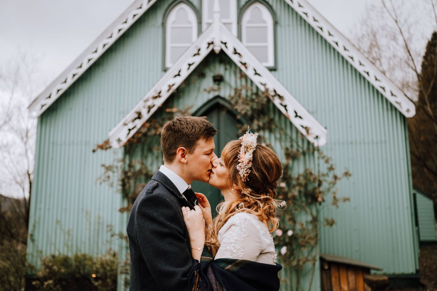 Romantic embrace between couple in front of mint green chapel during autumn wedding celebration.