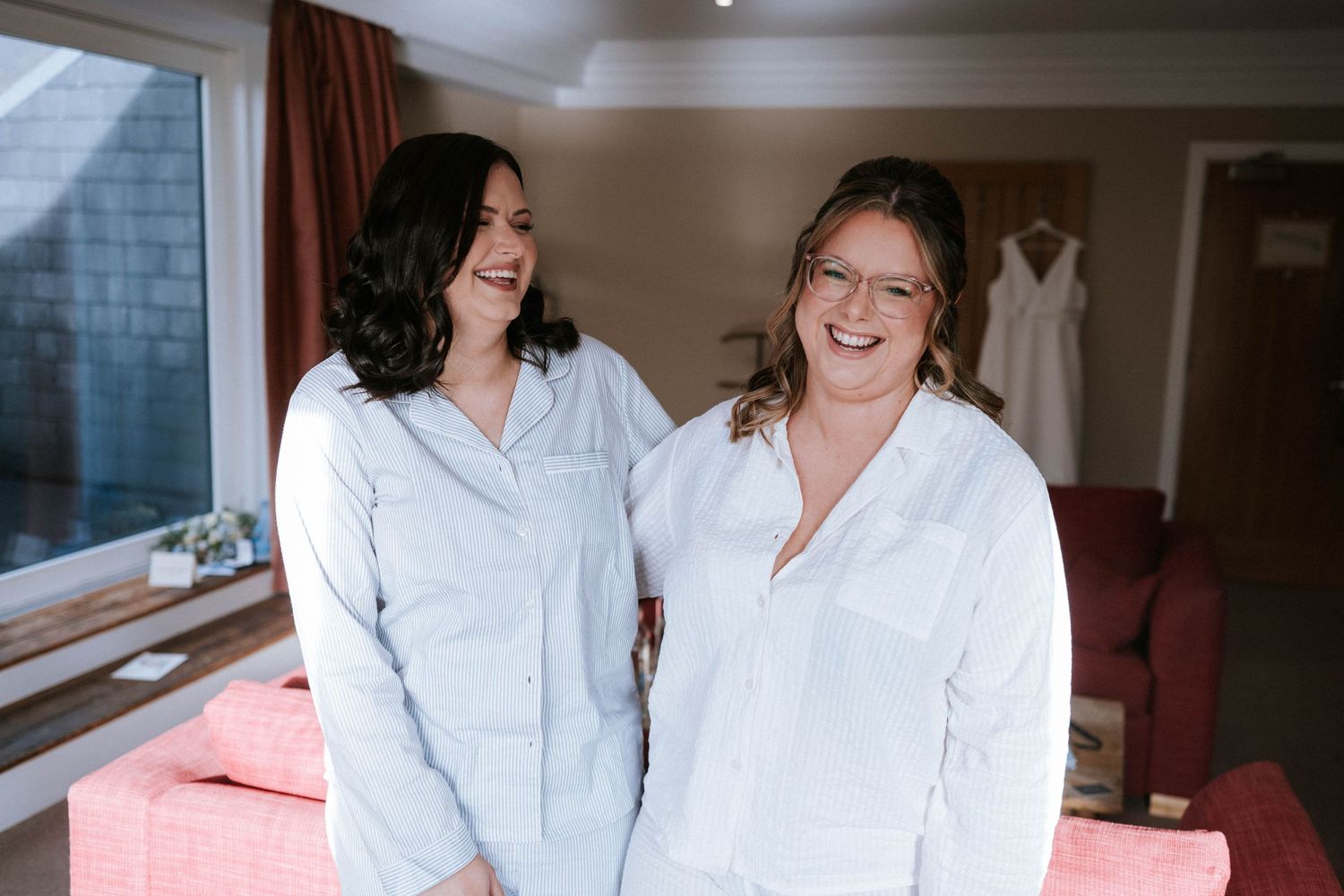 Two people in white robes sharing a candid moment during wedding preparations.