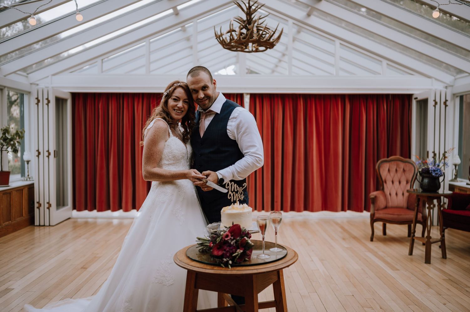 A wedding celebration inside an elegant white conservatory with red curtains and antique decor.