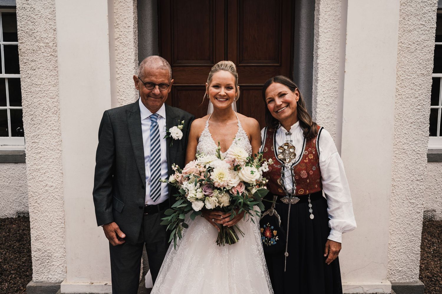 Wedding party poses in front of white building with wooden door.