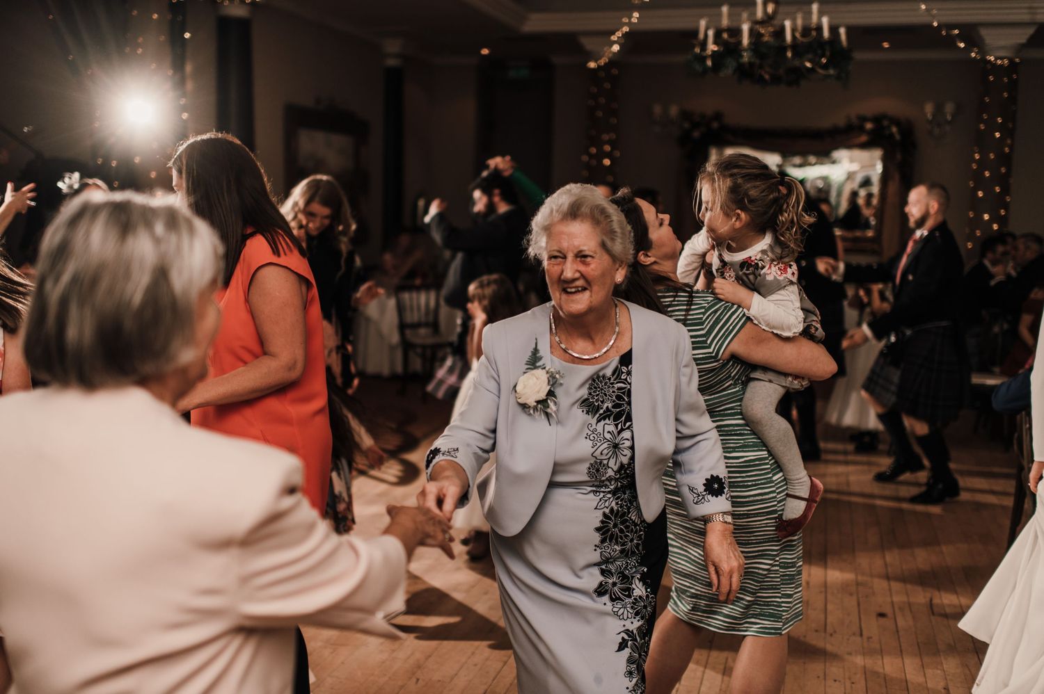 Wedding guests dancing and celebrating on a wooden dance floor during an evening reception.