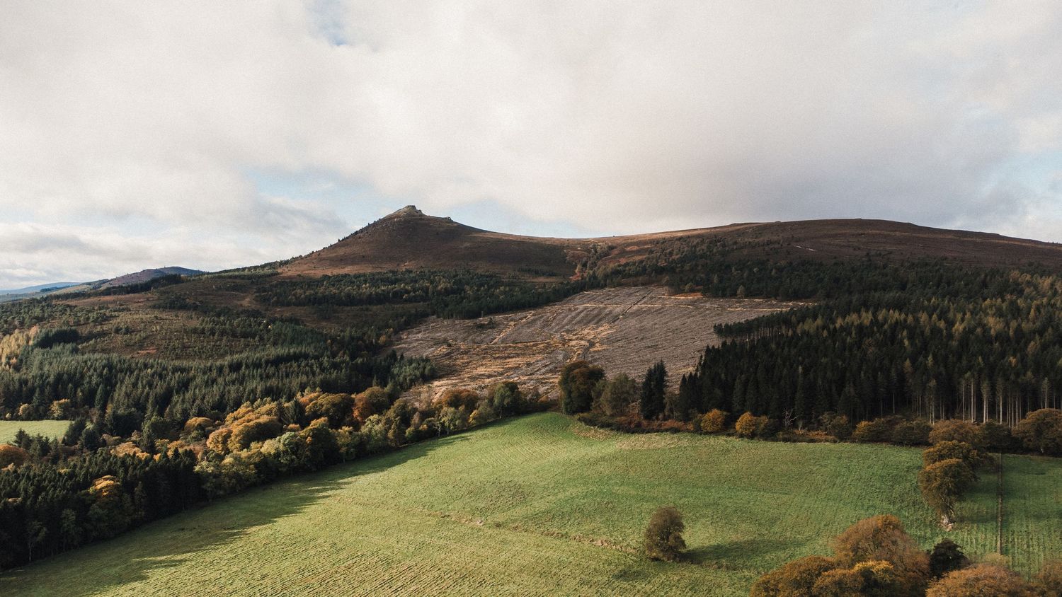 Rolling hills and mountains with forests and meadows under an overcast autumn sky.