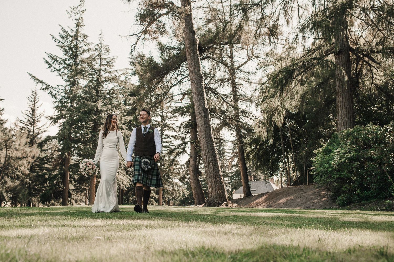 Couple walks hand in hand through majestic forest on their wedding day.