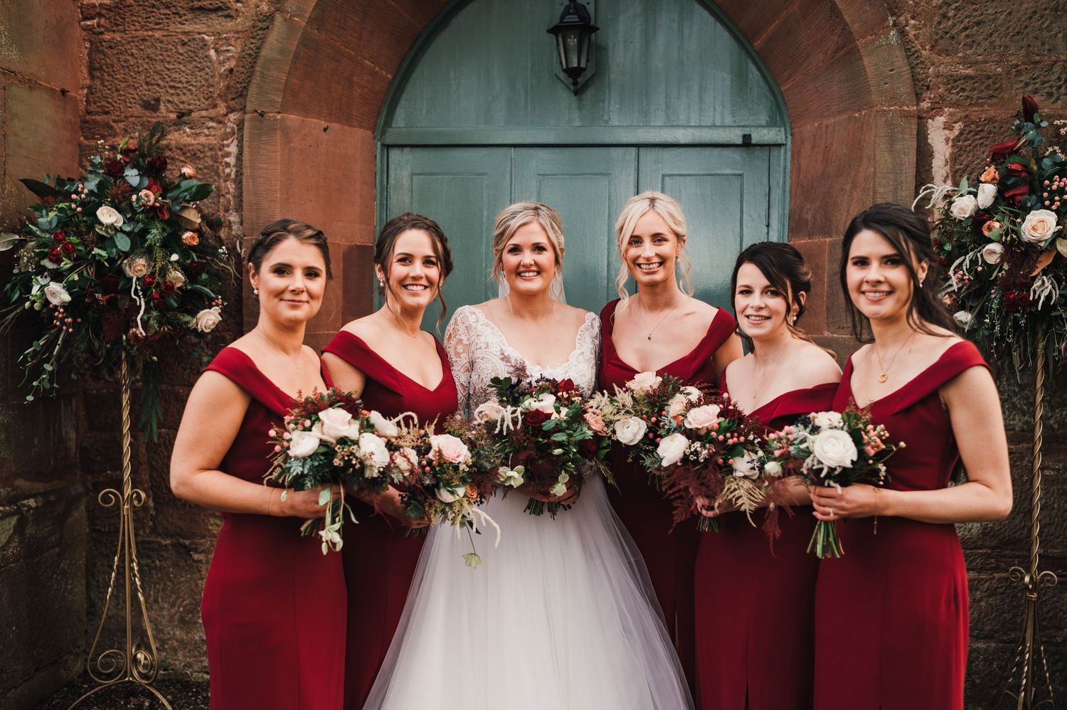 Bridal party in burgundy dresses and white gowns pose with floral bouquets.