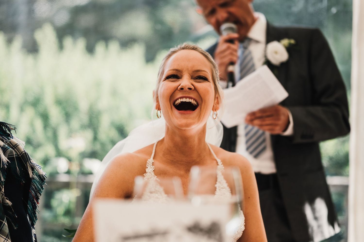 Candid reaction during wedding reception speeches with natural lighting.