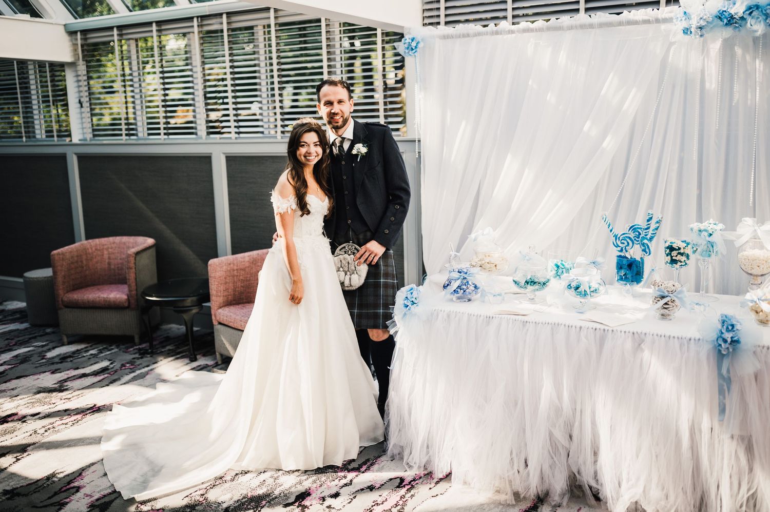 Wedding couple posing beside decorated dessert table with white and blue accents.
