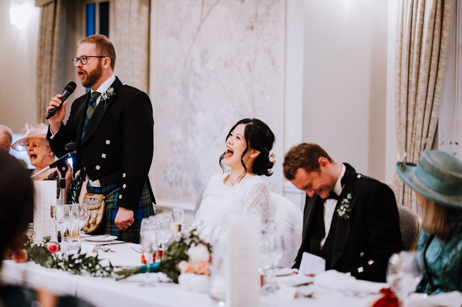 Speech being given during elegant wedding reception with floral table decorations.