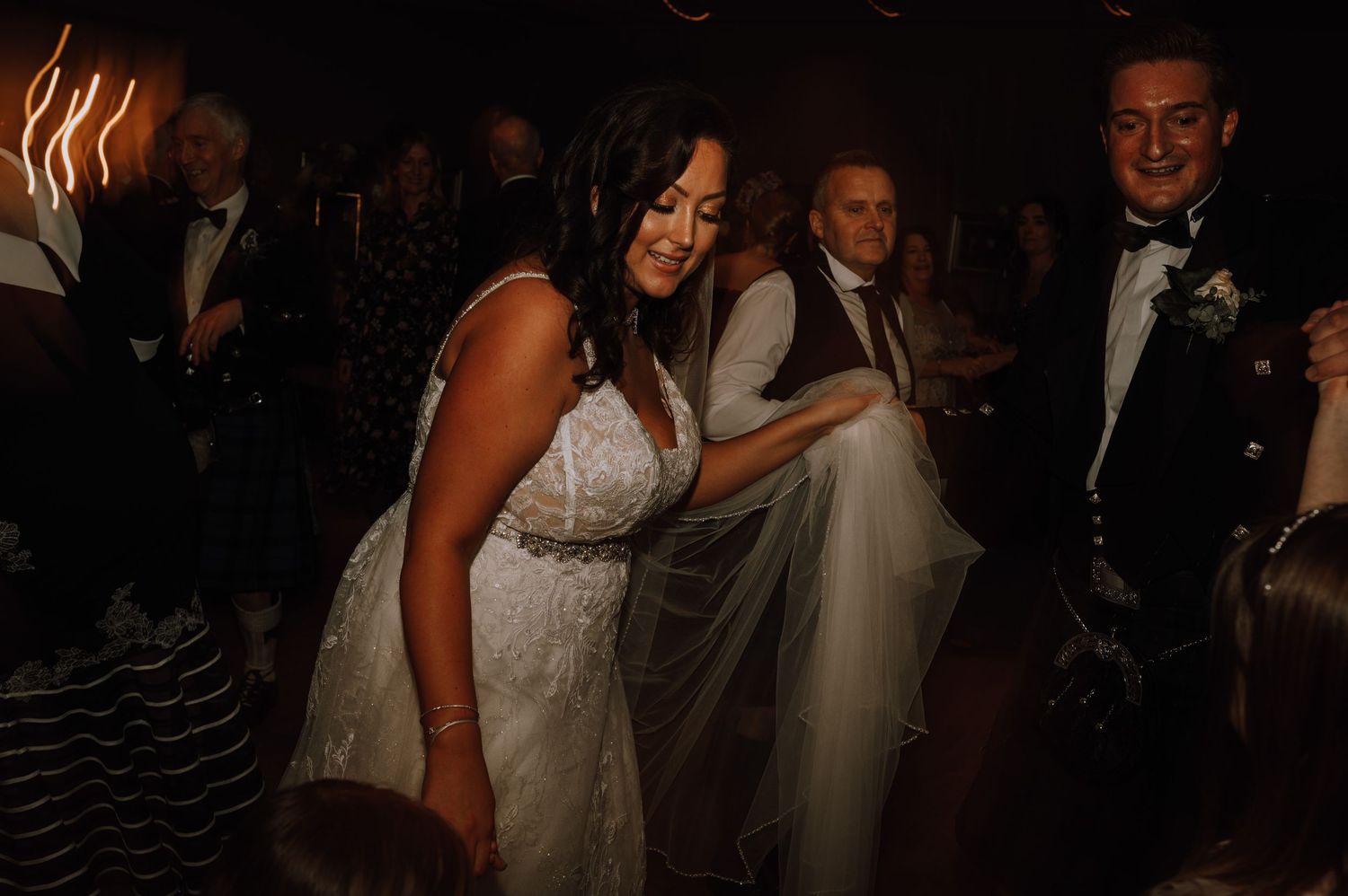 Wedding guests dance and celebrate at a dimly lit indoor reception venue.