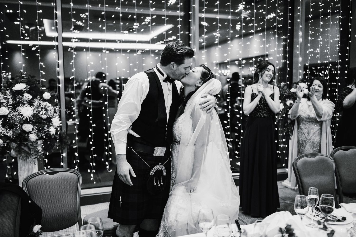 Black and white photo of romantic moment at wedding reception with fairy light backdrop.