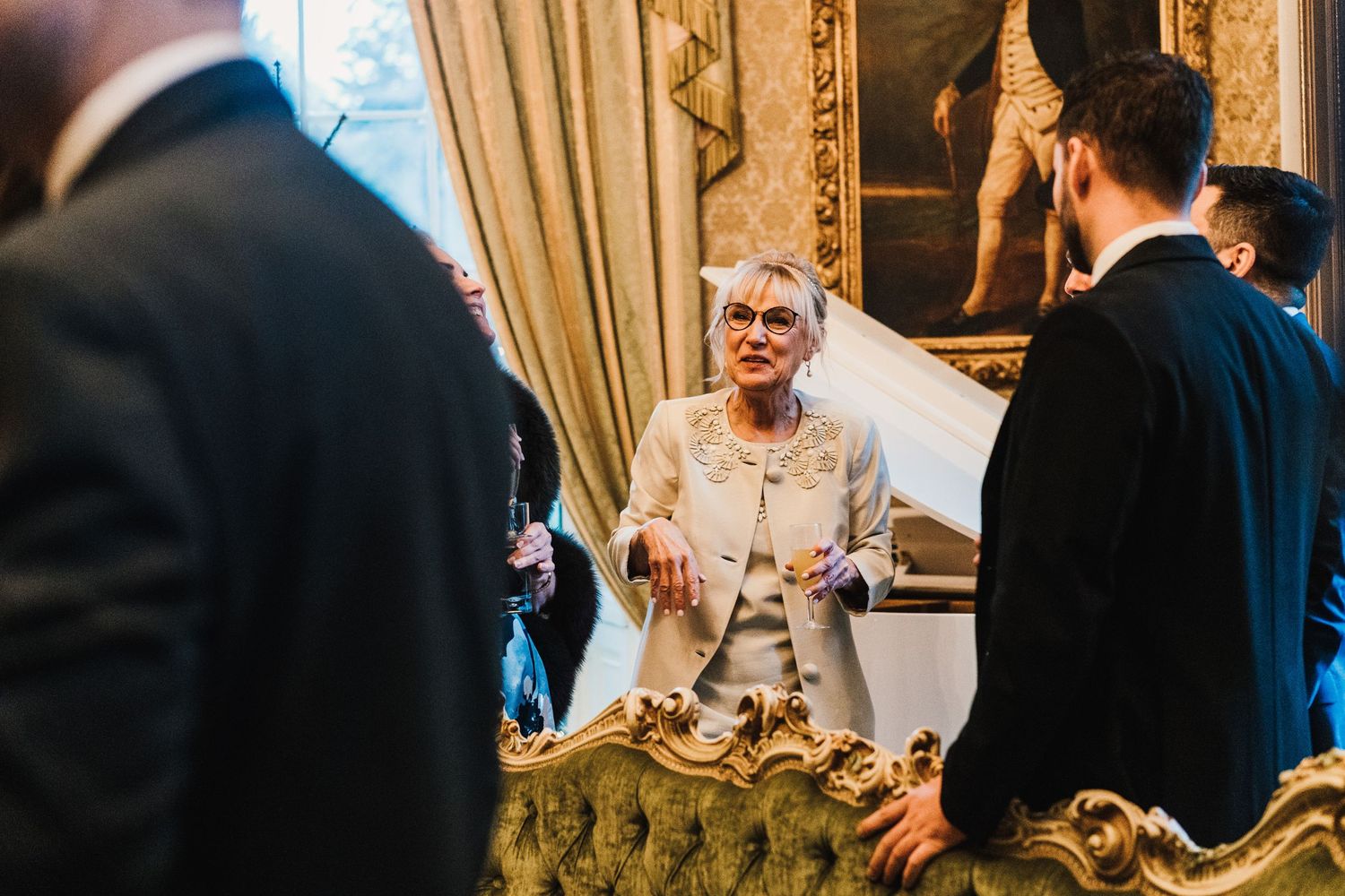 Wedding guests mingle and socialize in an ornate room with elegant curtains and decor.