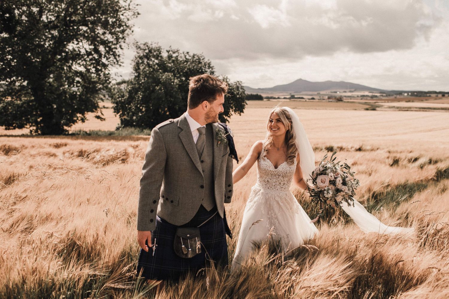 A wedding couple walks hand in hand through swaying wheat fields on their special day.