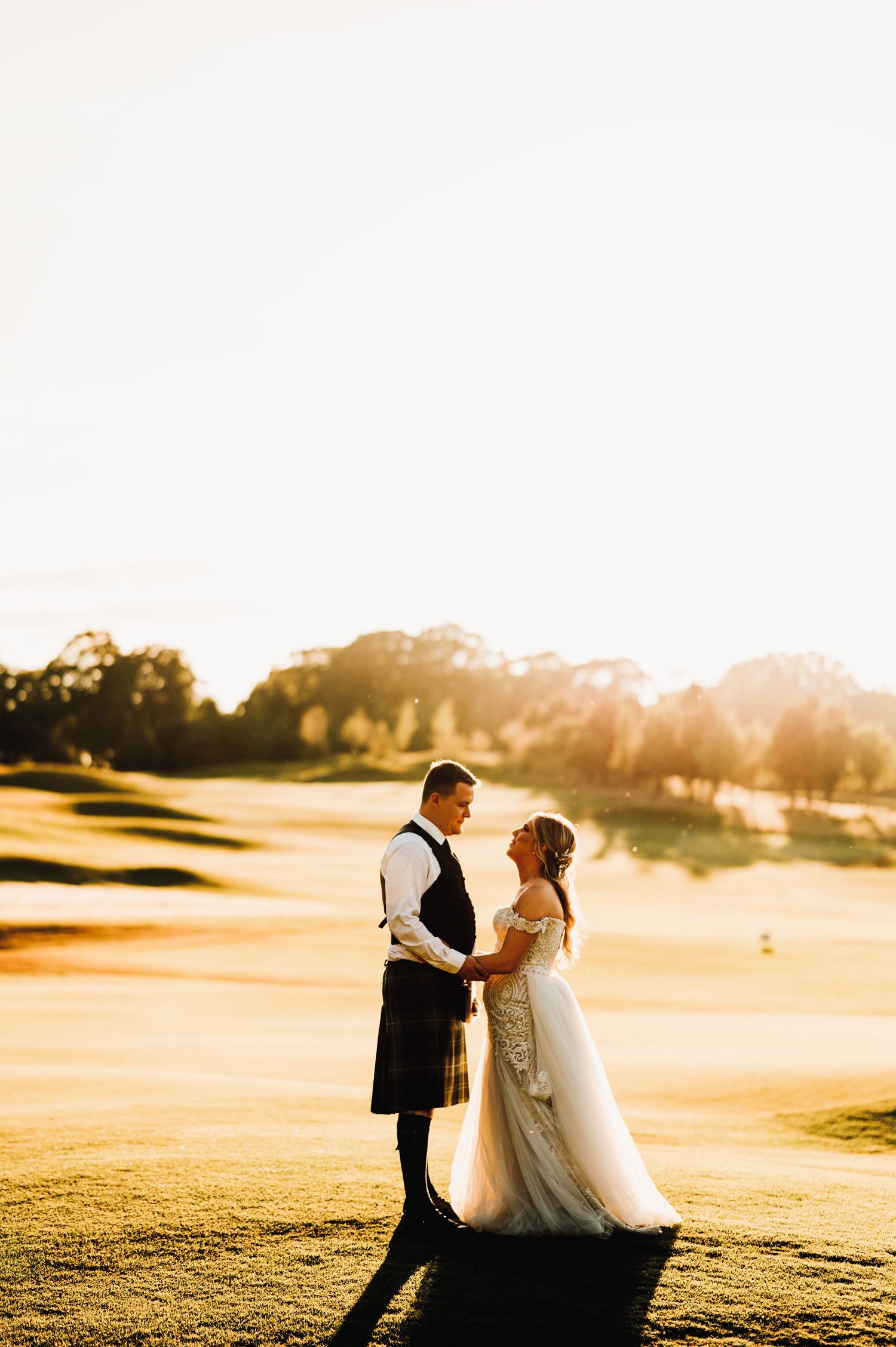A romantic sunset portrait of a couple in wedding attire on a golf course.