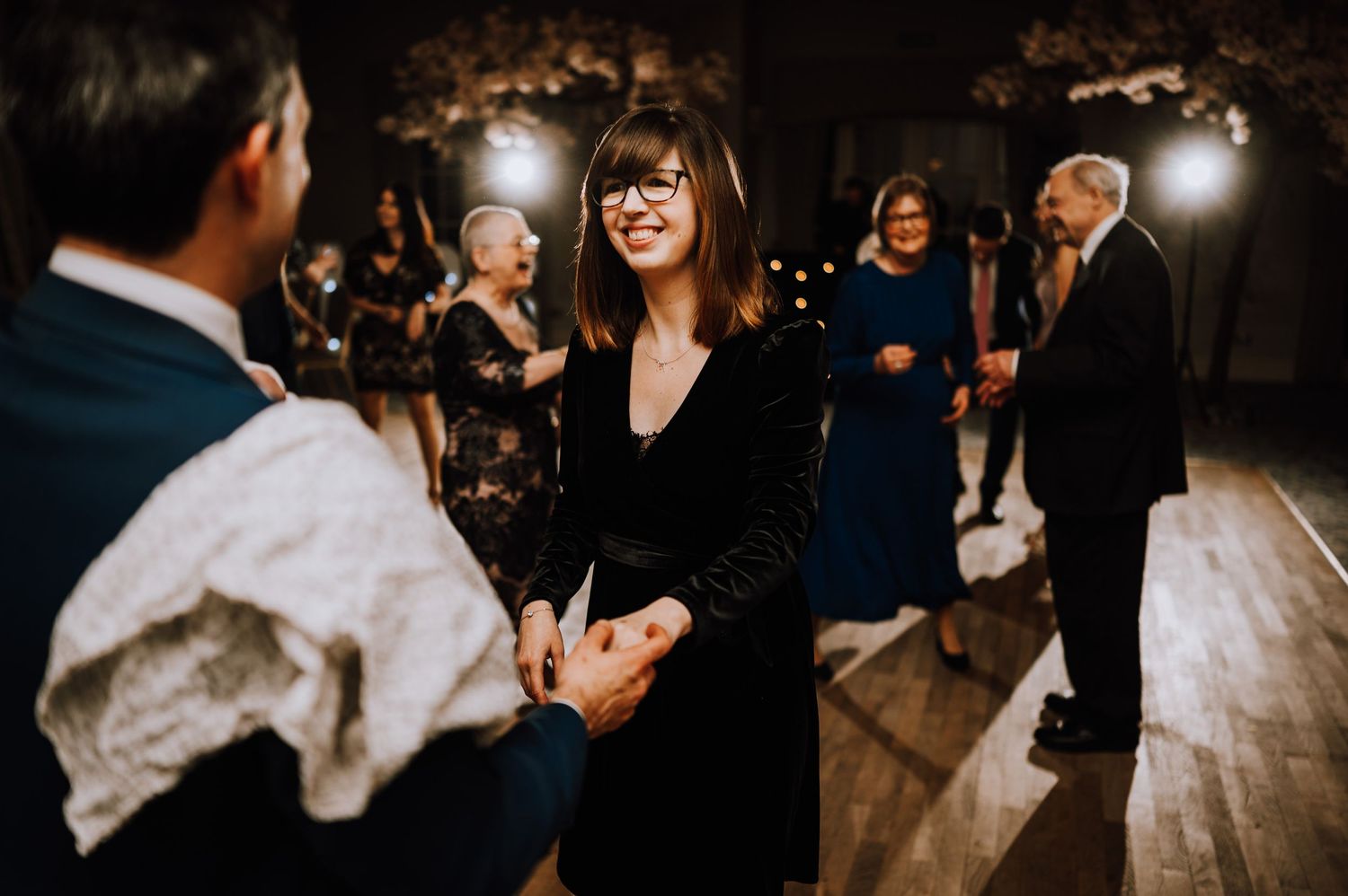Guests dancing at an evening reception with atmospheric lighting and wooden floors.
