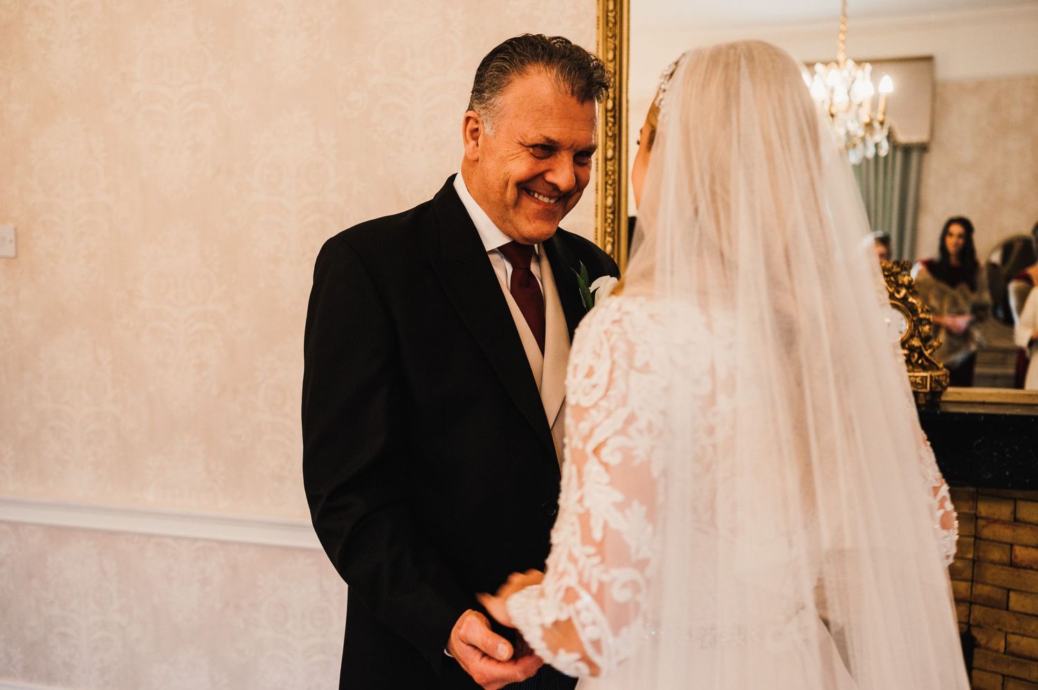 A touching moment between a bride in lace and someone in a black suit during a wedding ceremony.