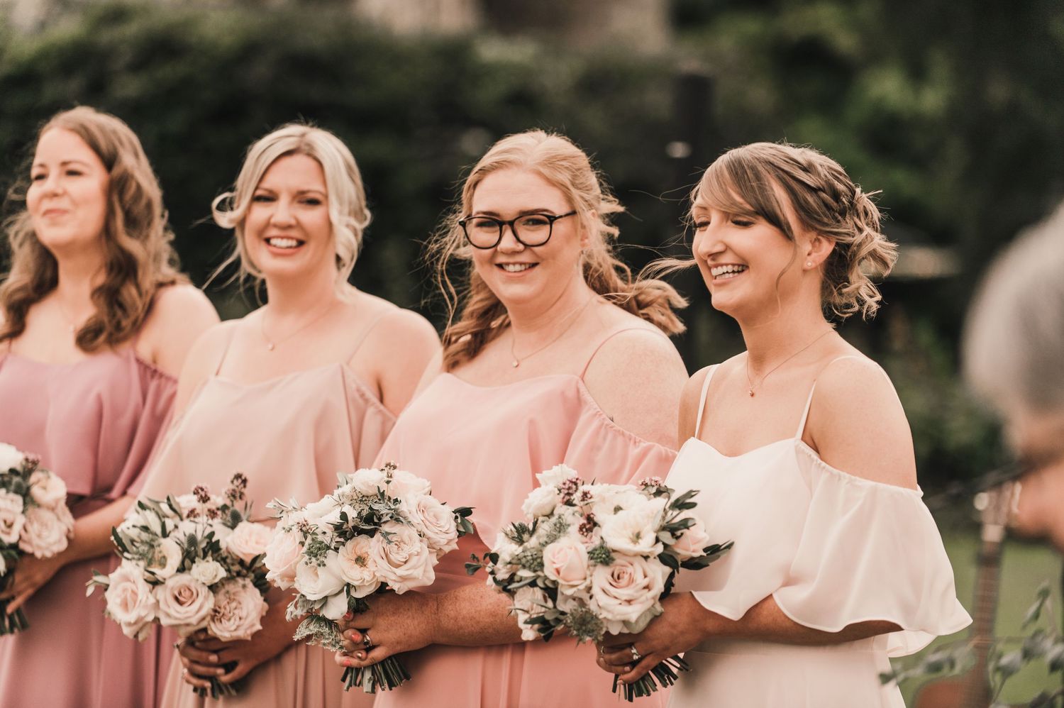 Bridesmaids in matching pink dresses hold matching floral bouquets during wedding celebration.