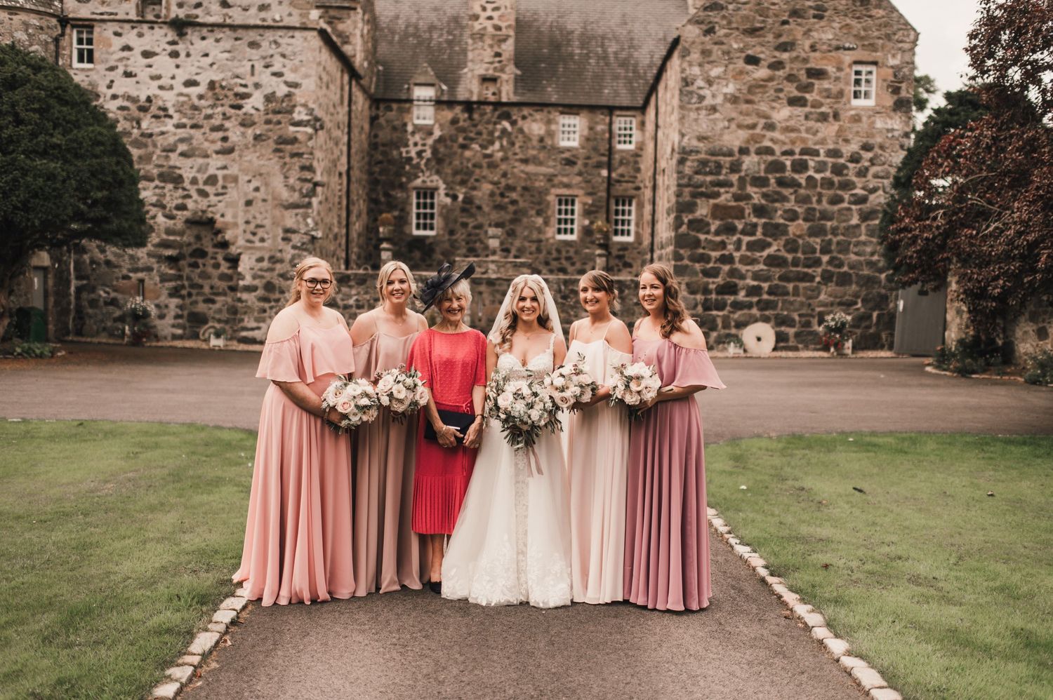 Wedding party in pink dresses posing together outside a Scottish stone castle.