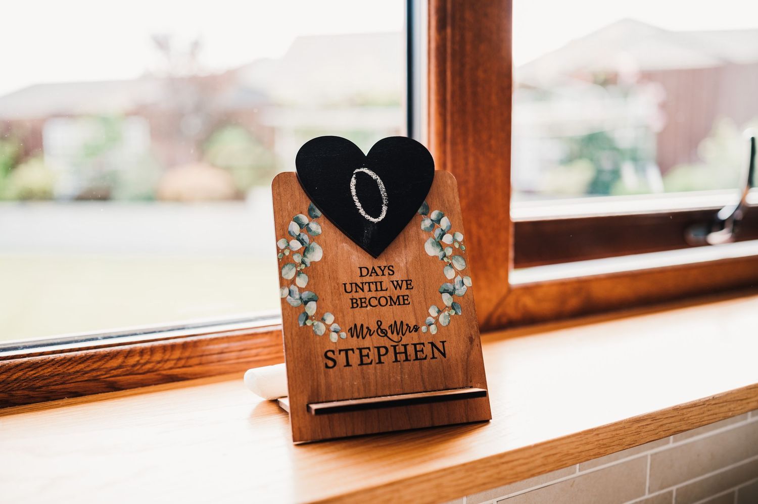 Black heart-shaped wedding sign with names displayed on wooden windowsill.