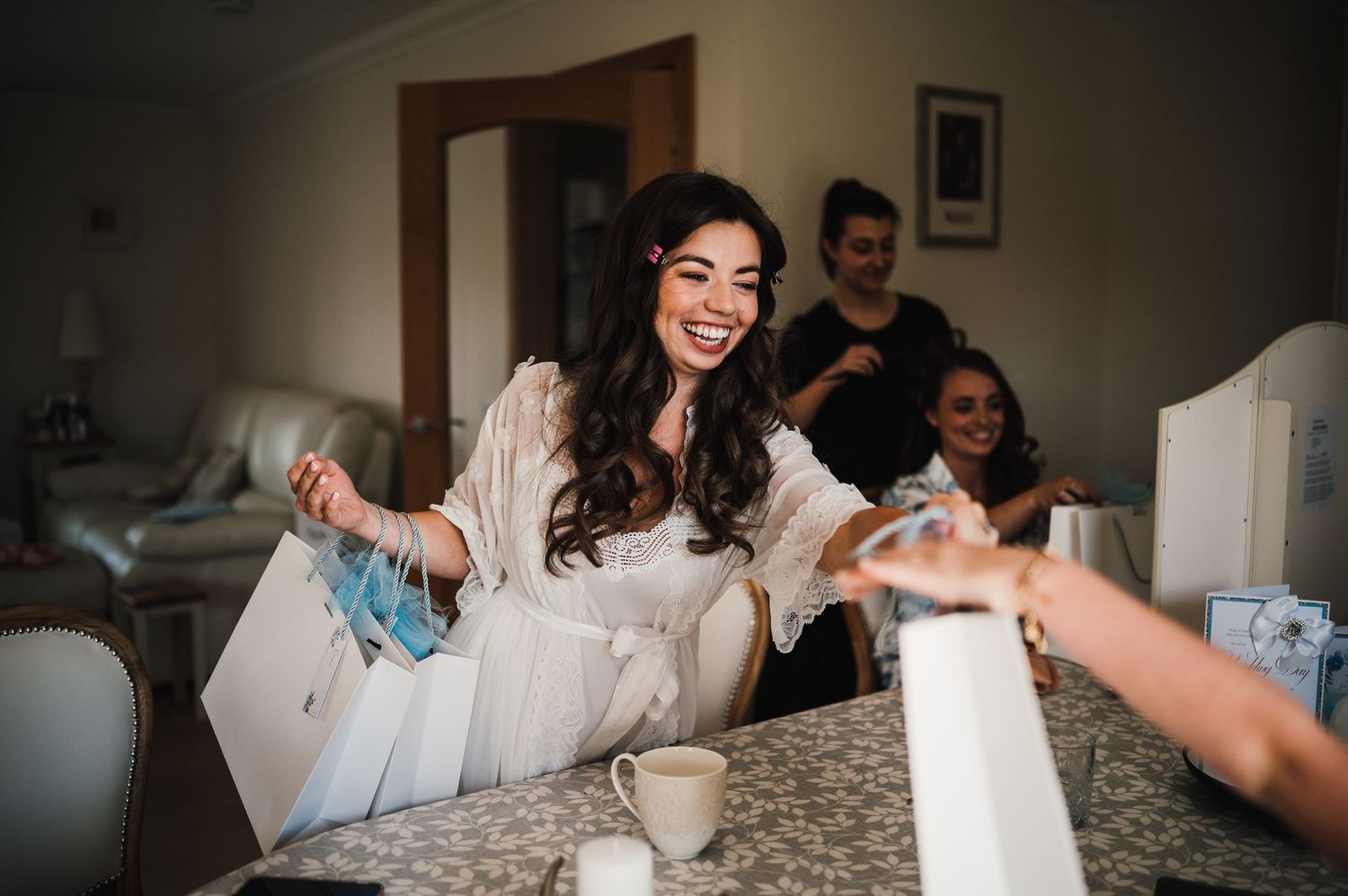 A joyful celebration during a wedding preparation as someone in white robe opens gifts at a table.