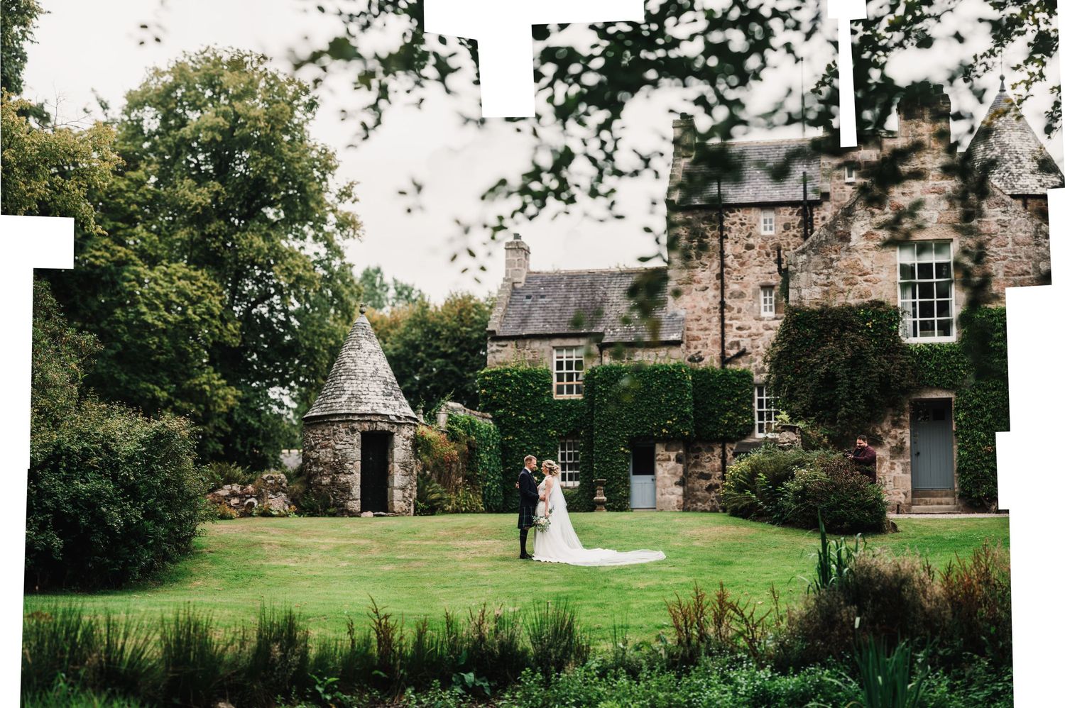 Wide shot of Scottish stone estate with manicured gardens and wedding celebration.