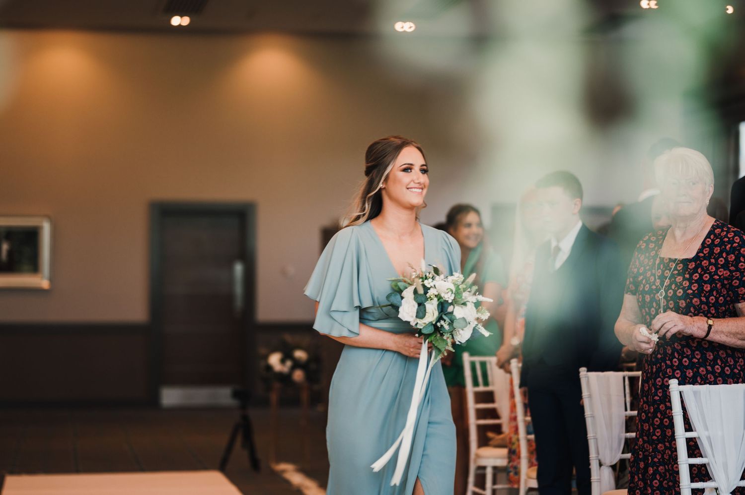 Bridesmaid in pale blue dress carries bouquet during wedding processional.