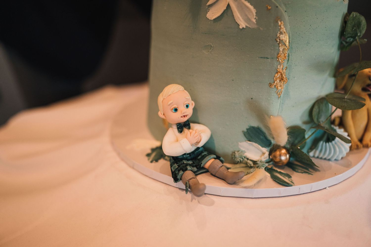 Closeup of whimsical cake decorations featuring small figurines and botanical elements.