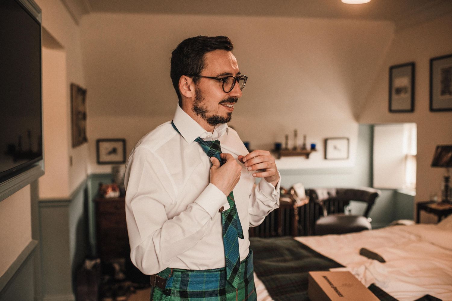 Someone adjusting a tie while wearing formal attire with a traditional Scottish kilt.