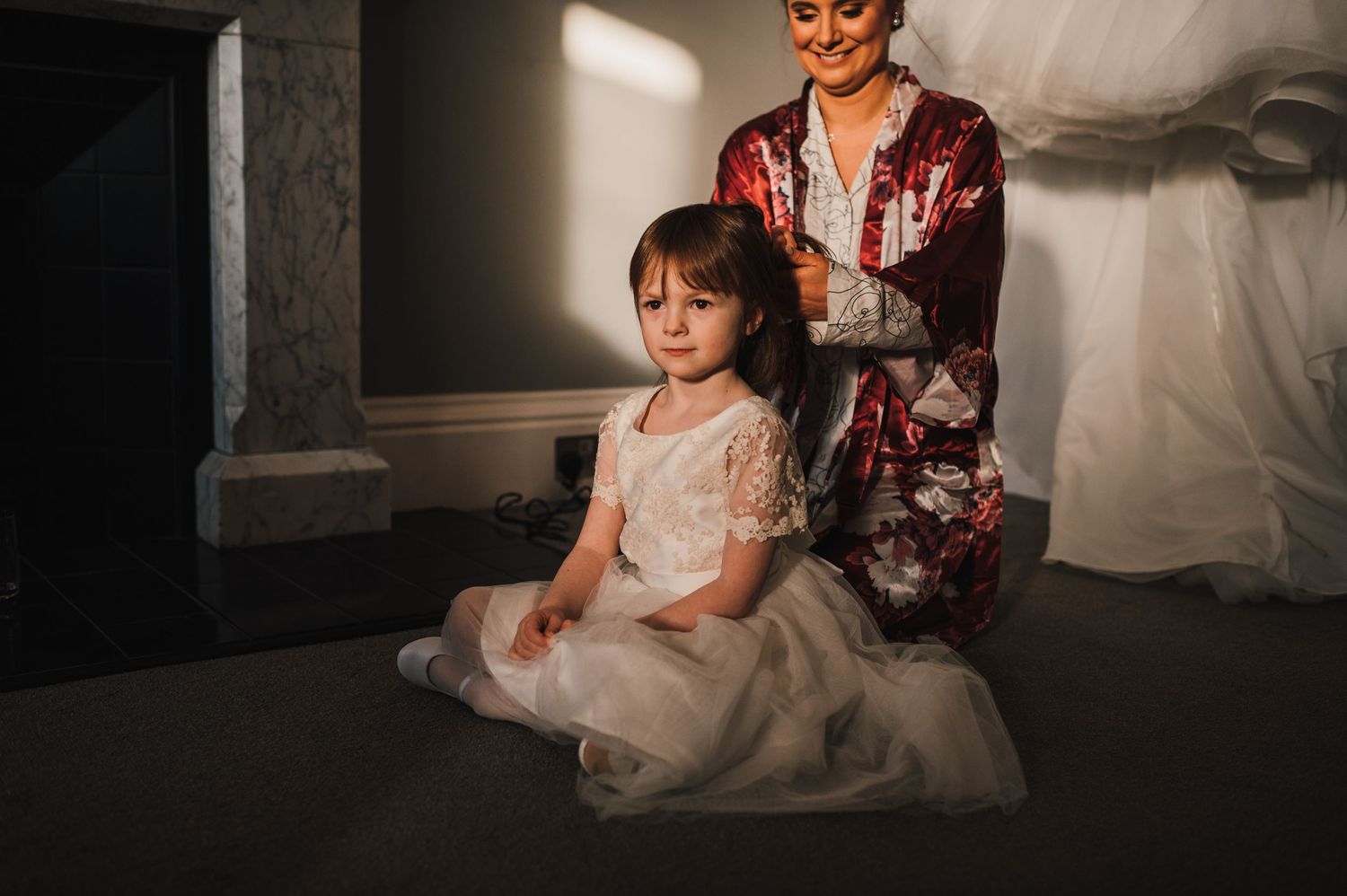 A candid moment in soft lighting shows preparations in a wedding dress.