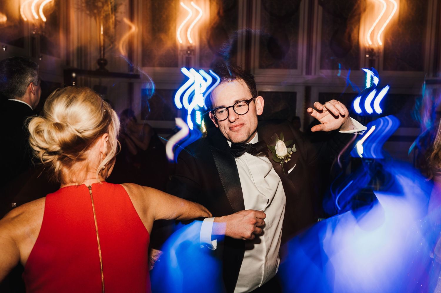Enthusiastic party guests dancing under blue lighting at formal event.