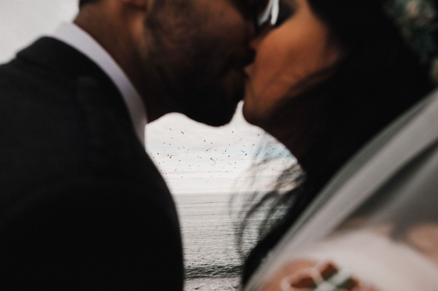 A romantic kiss captured through a veil during a rainy wedding ceremony.