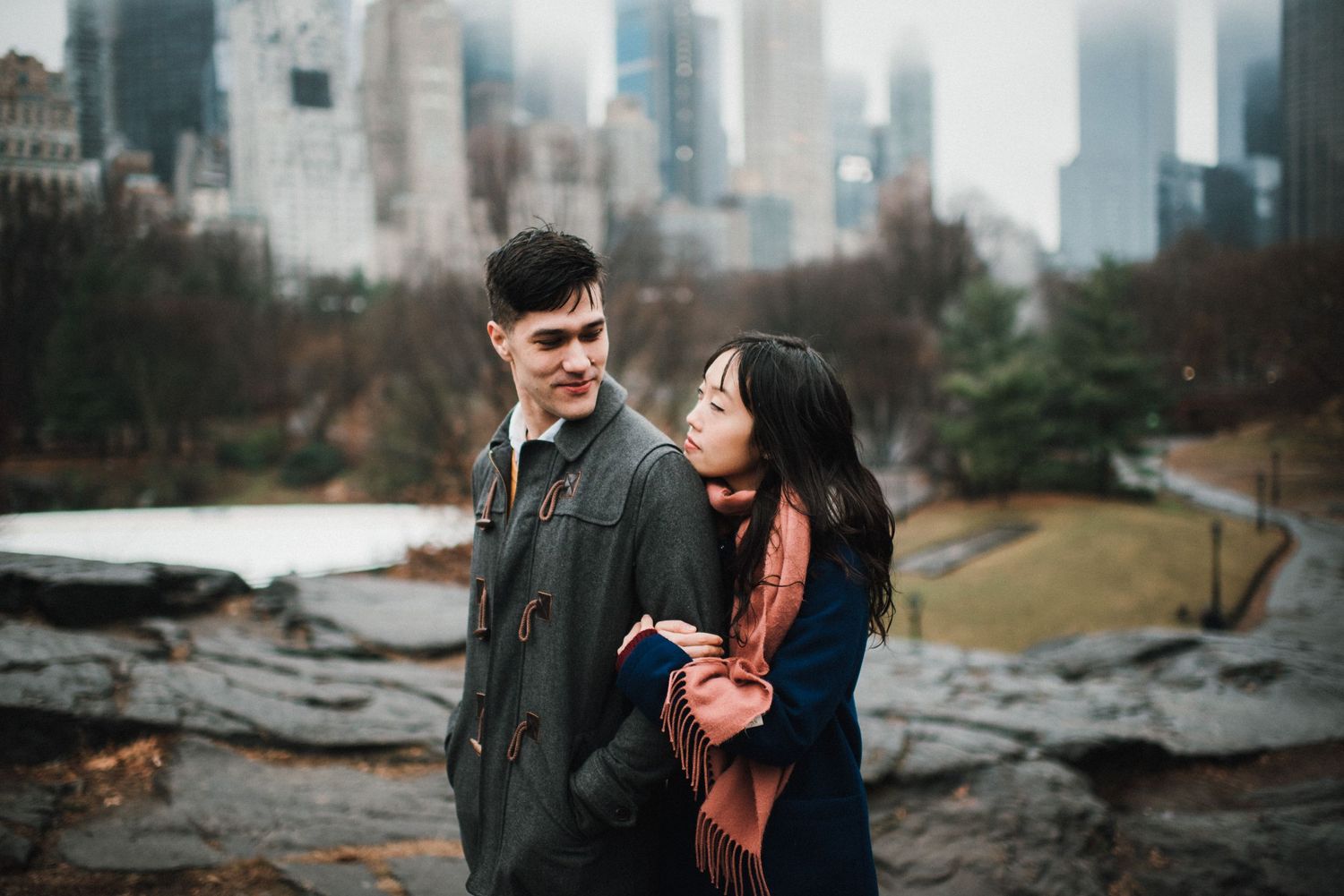 A couple shares an intimate moment on rocky terrain with the Manhattan skyline as their backdrop.