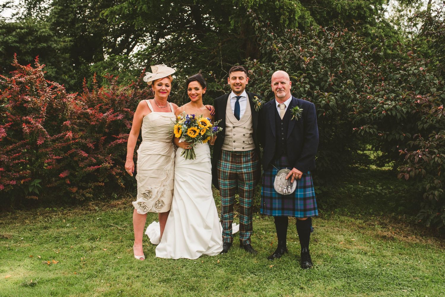 Wedding party poses on grass with traditional Scottish kilts and formal attire.