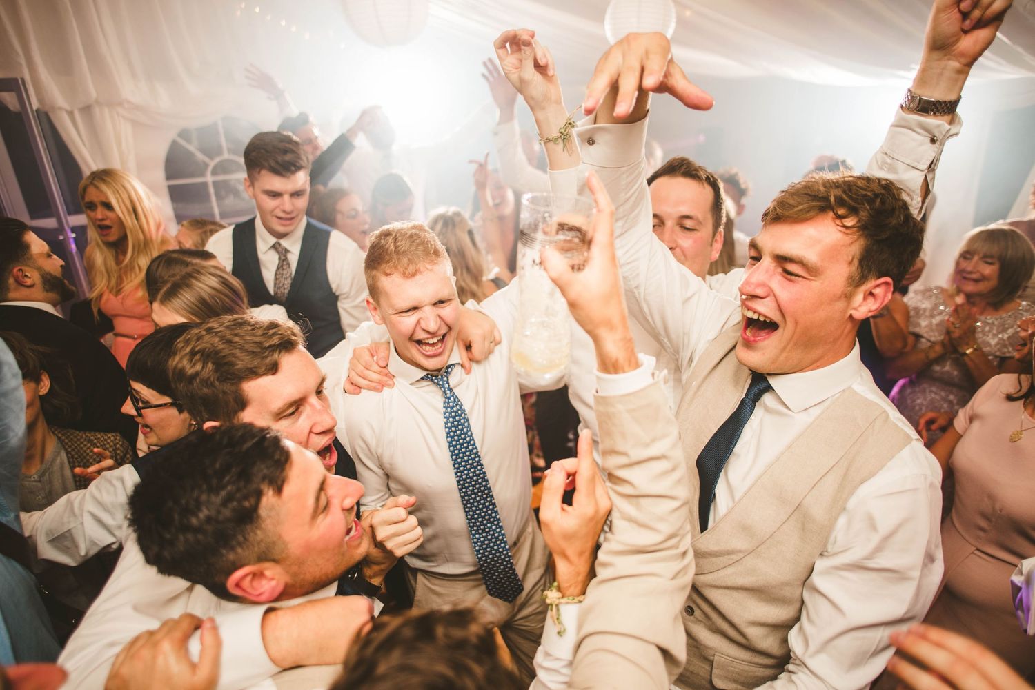Energetic wedding reception party with guests dancing and jumping in celebration.