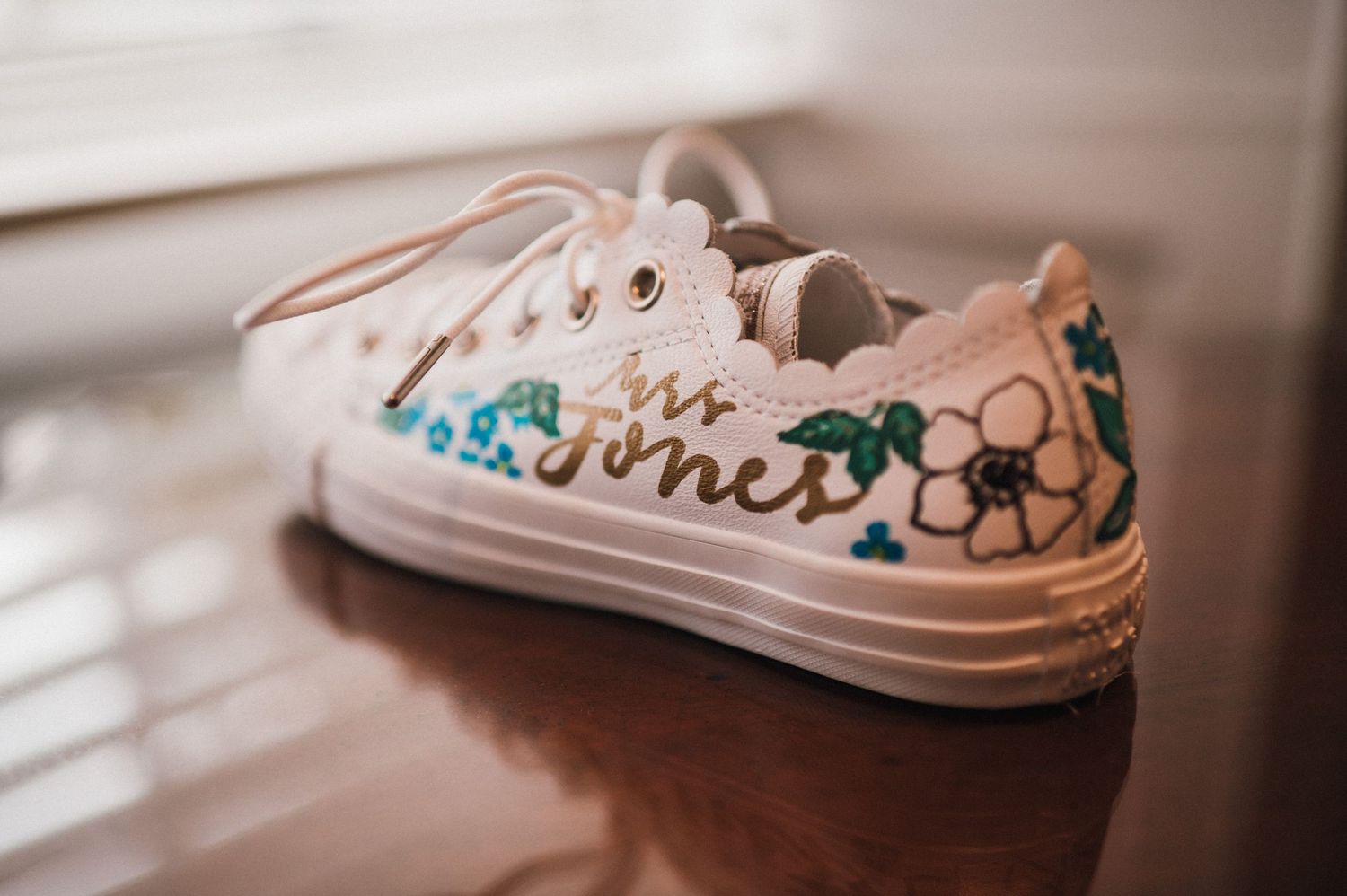 White canvas sneaker decorated with blue and green floral designs sitting on wooden surface.