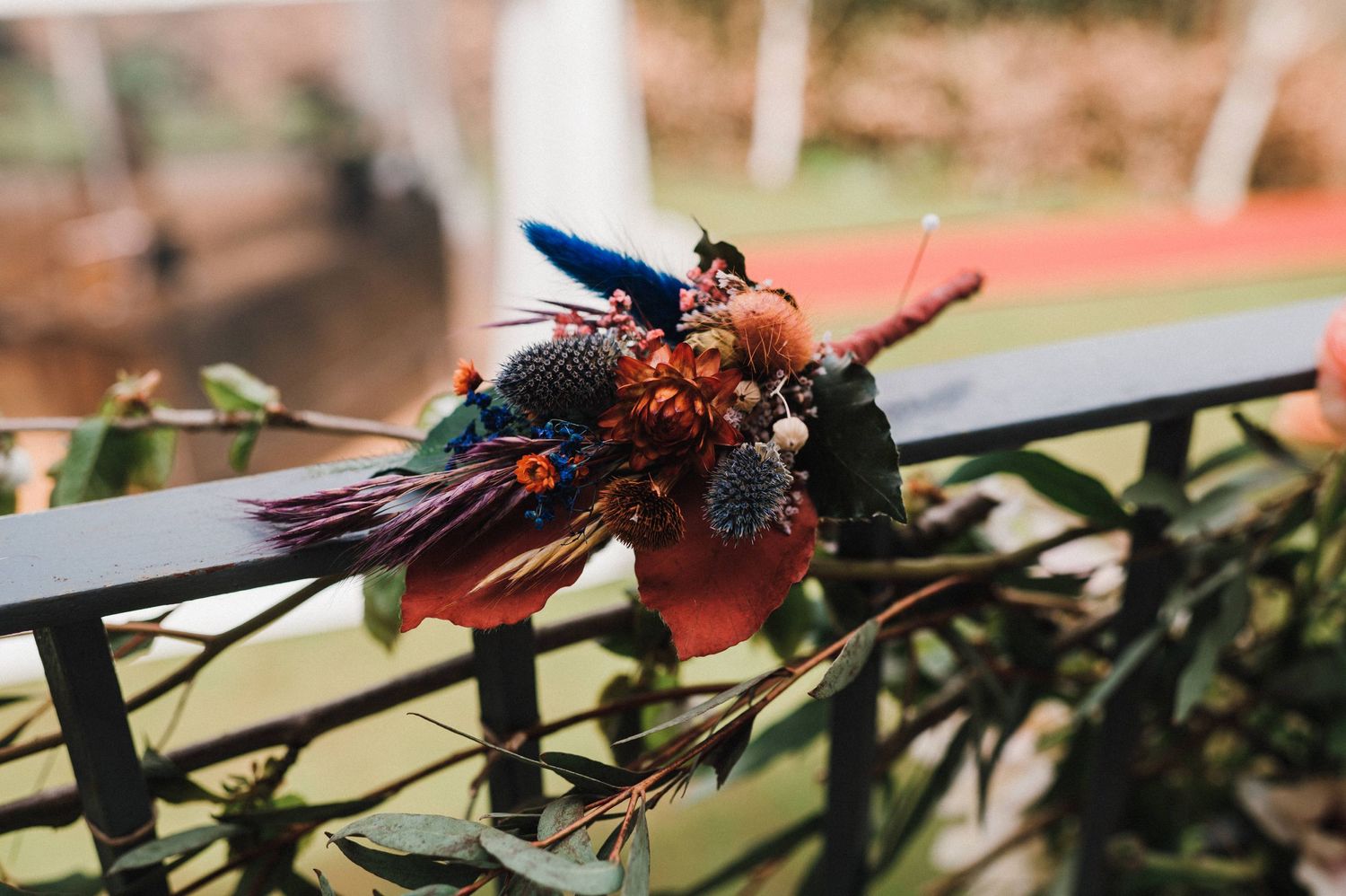 Decorative floral arrangement with blue feathers and dried flowers on a railing.