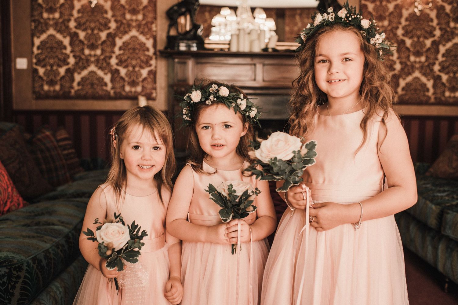Three young attendants in pink dresses with flower crowns holding bouquets.