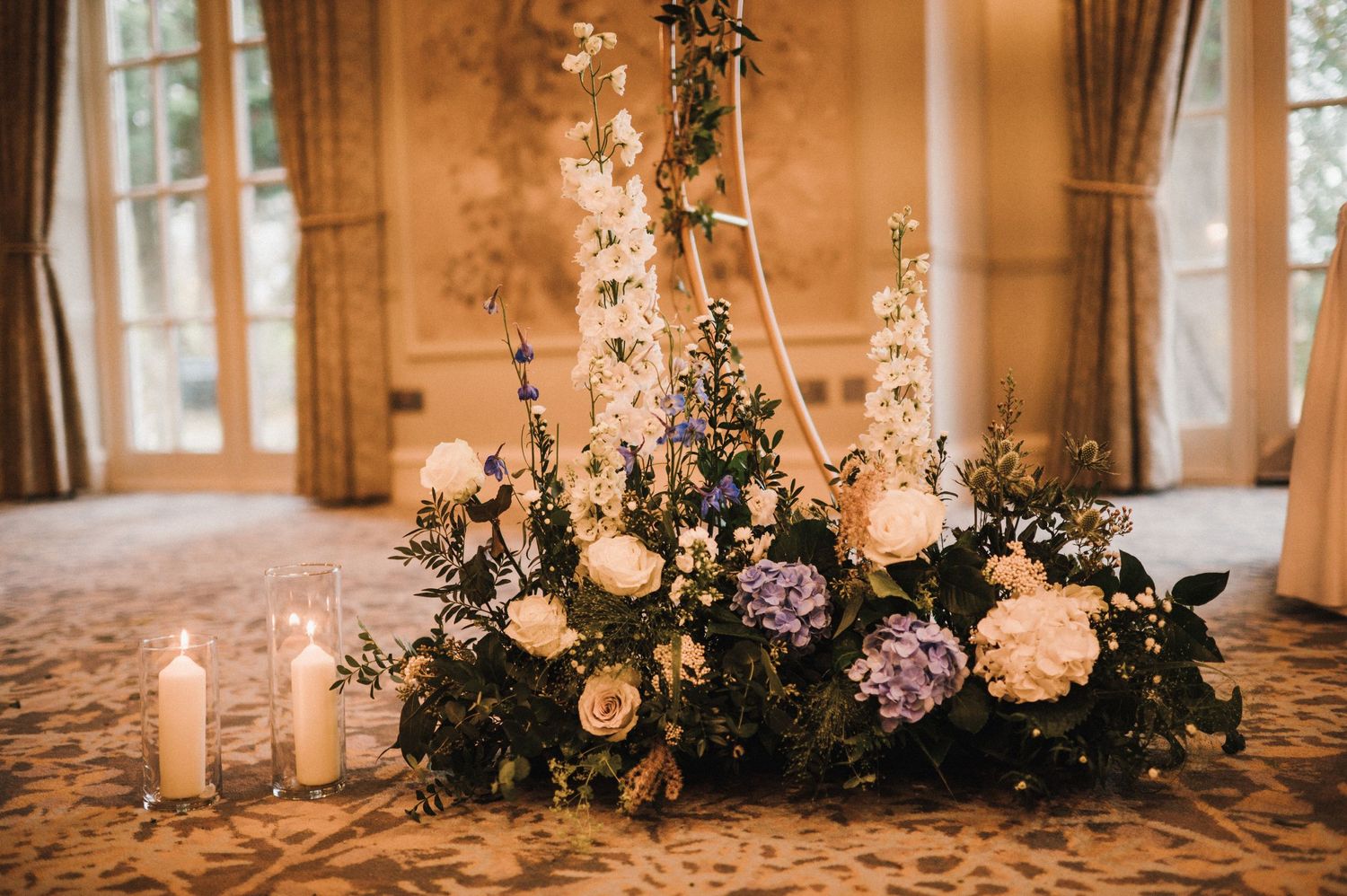 Elegant floral centerpiece with white roses, hydrangeas, and candles on a patterned tablecloth.