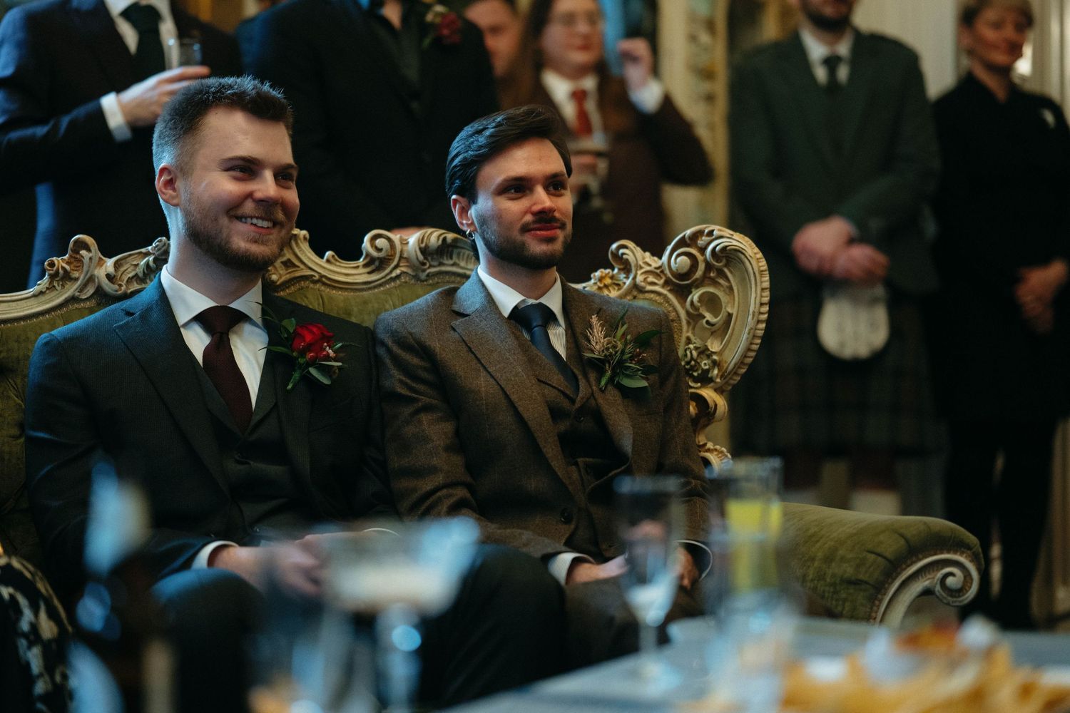 Guests seated in ornate room with gilded furniture during formal event.