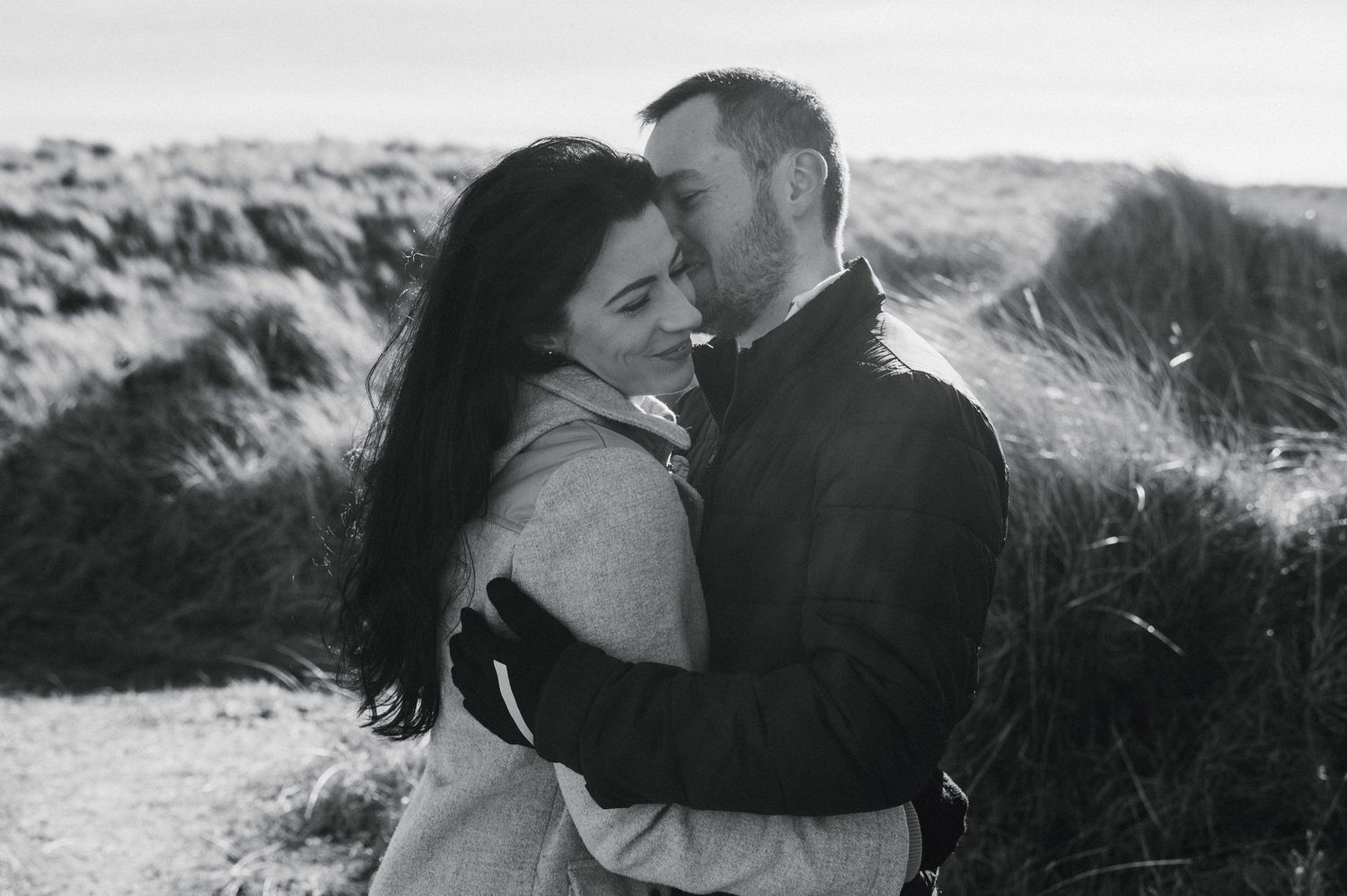 A romantic couple embraces in a black and white photo series set against natural outdoor backdrops.
