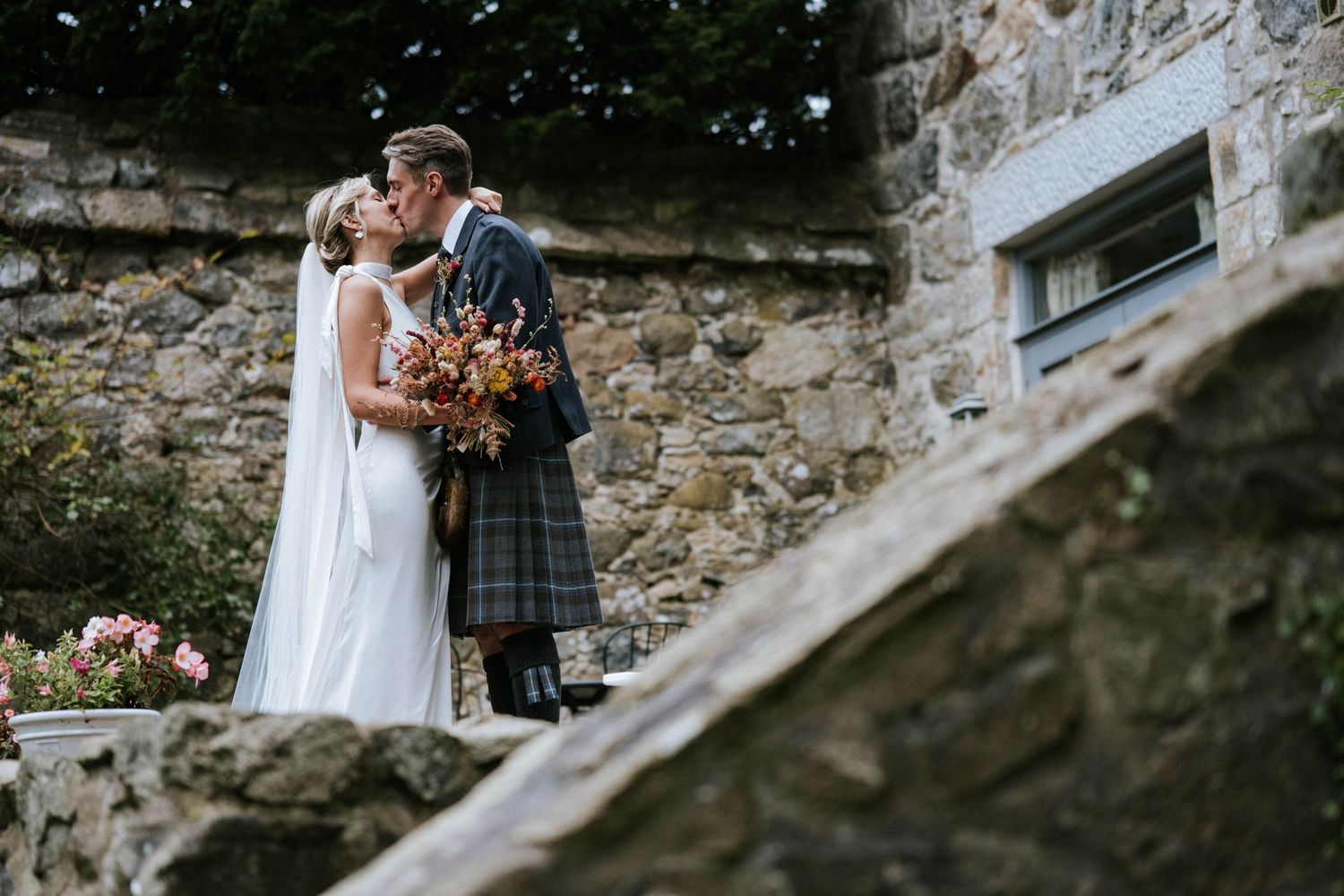 A couple embraces on stone steps during their Scottish-themed wedding.