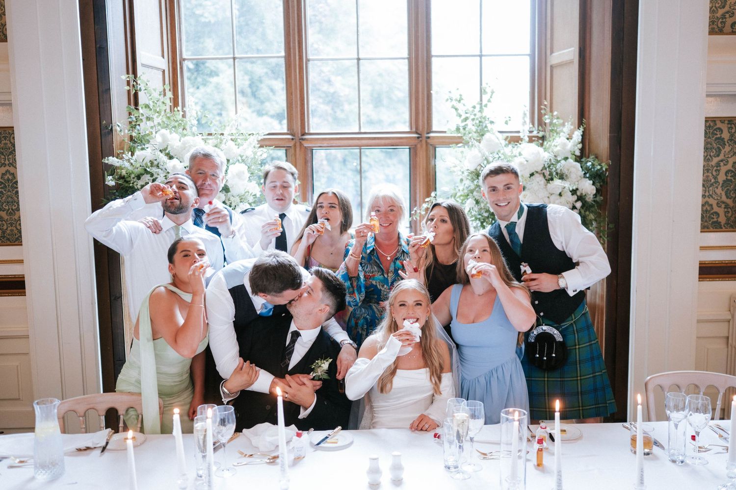 Wedding reception guests react joyfully during celebrations in a bright dining room.