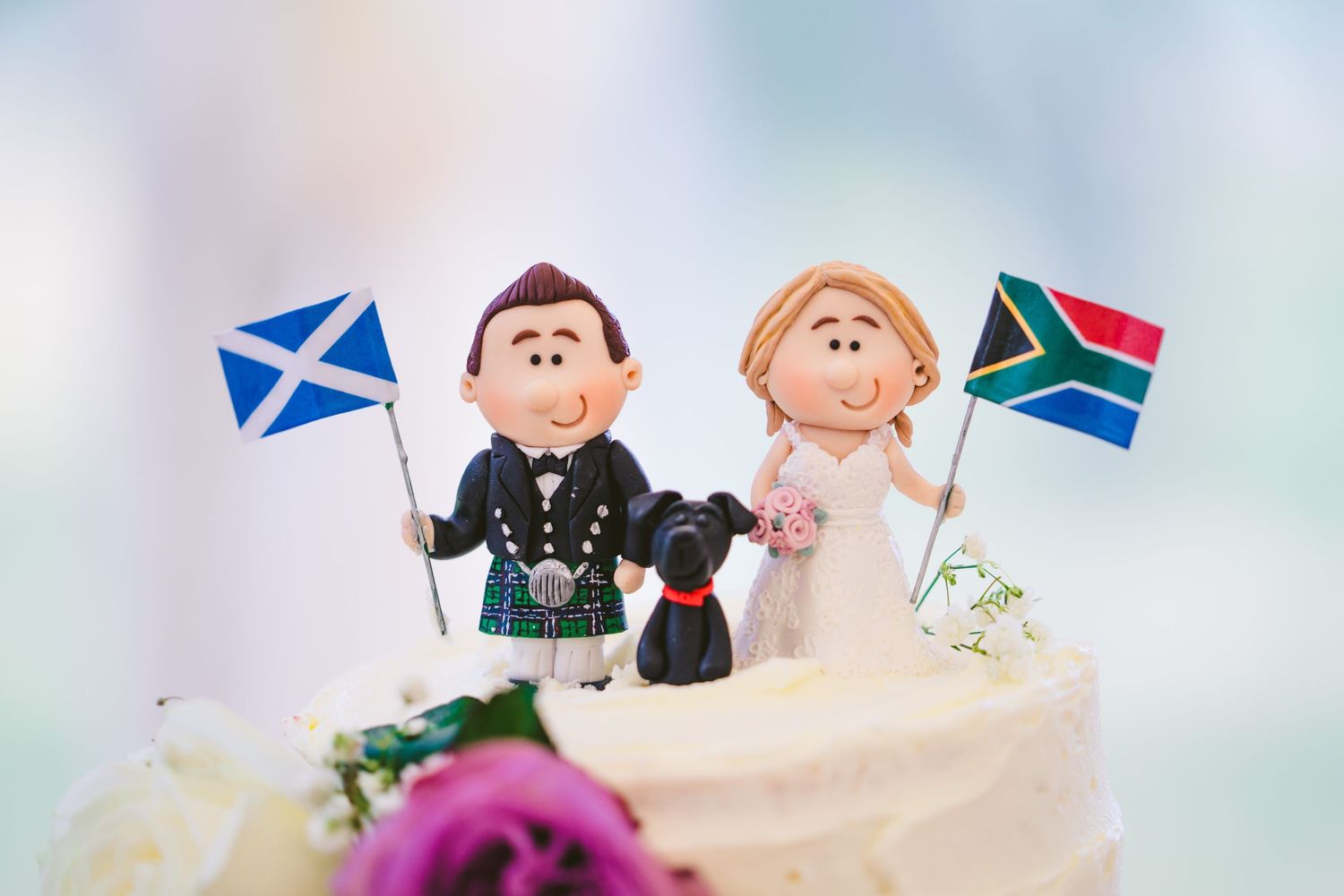 Wedding cake toppers featuring Scottish and South African flag details.