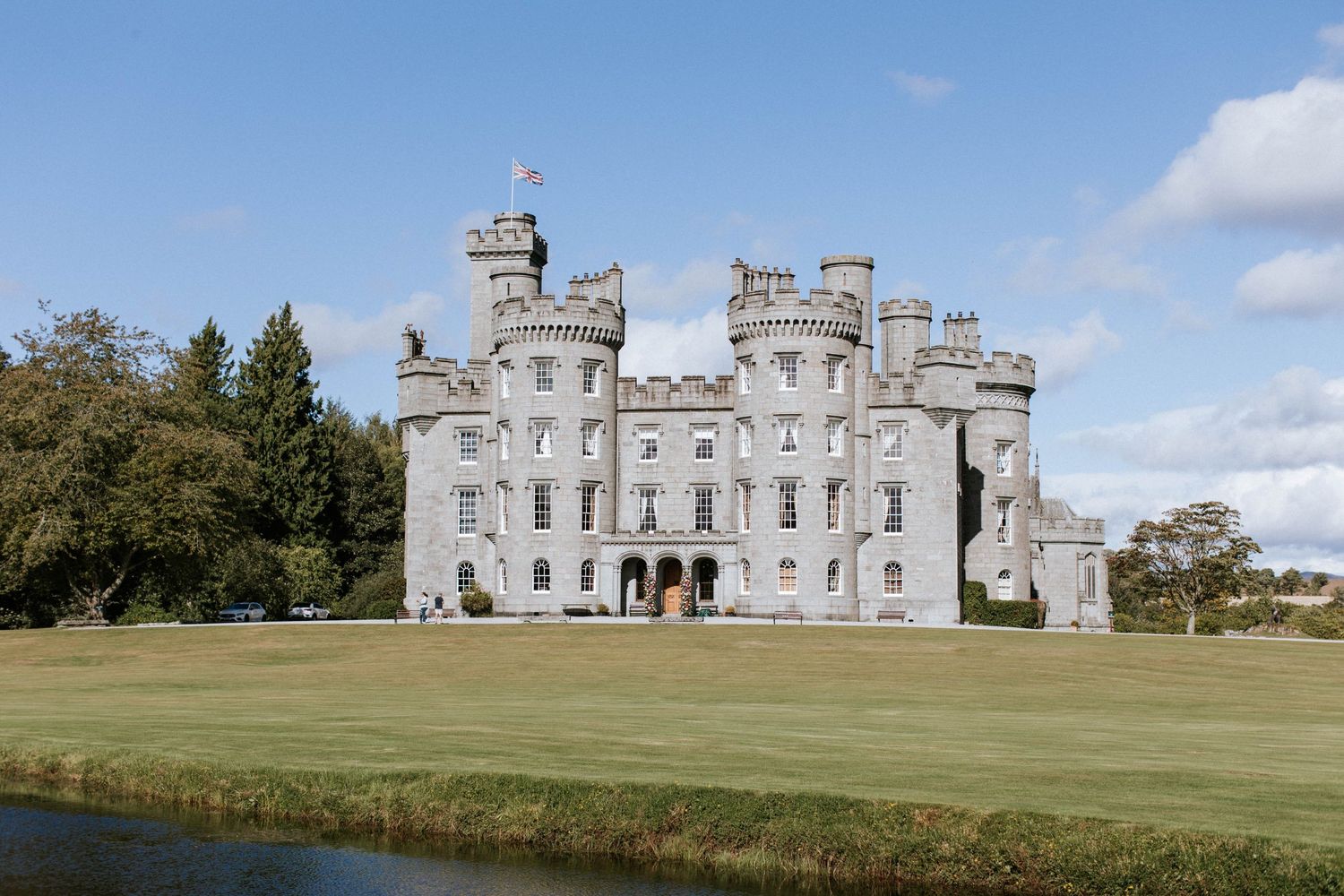 Panoramic view of a grand Scottish castle with Gothic architecture set against blue skies.
